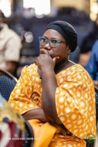 a woman in glasses and a yellow shirt with her hand on her chin